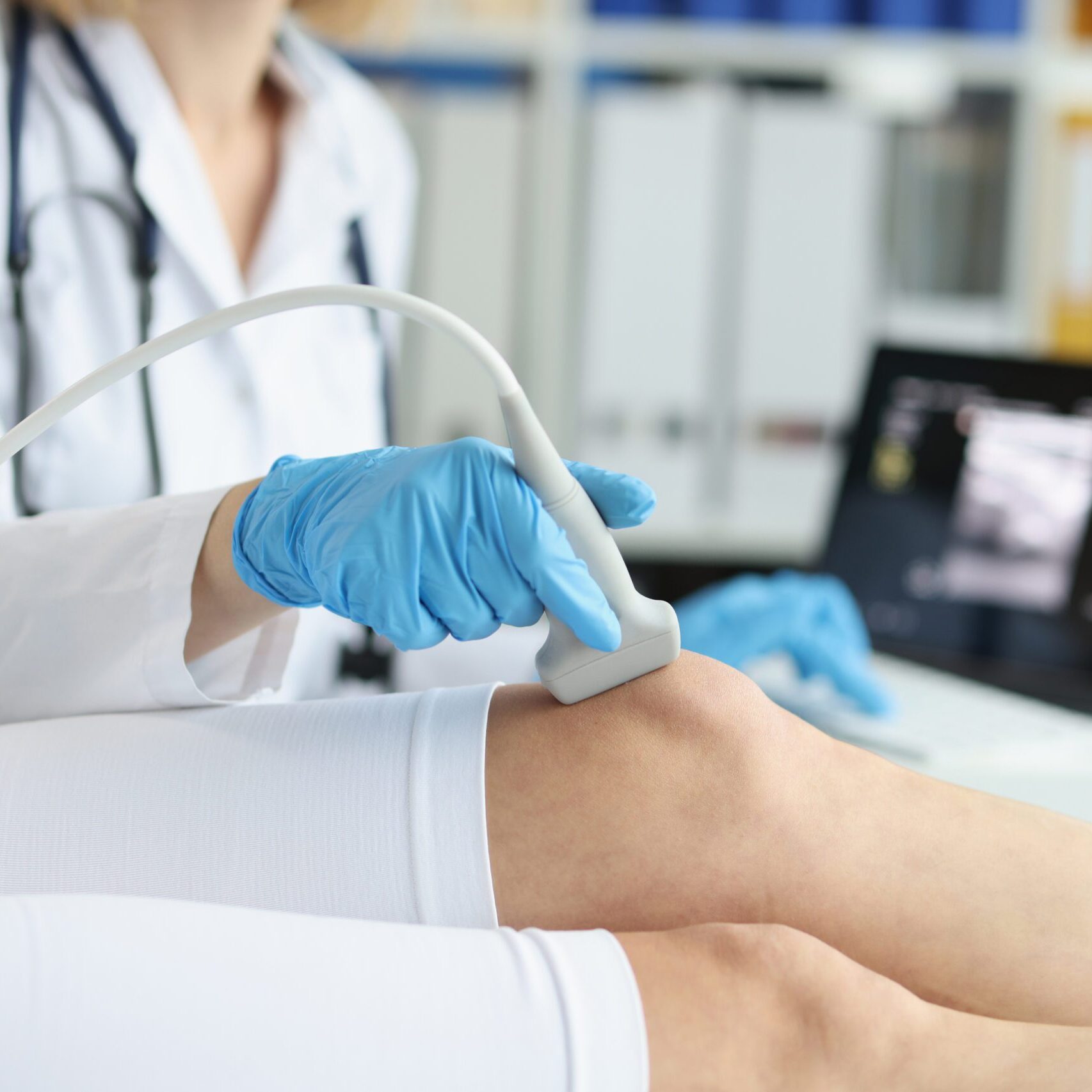 Orthopedic doctor makes ultrasound examination of patient knee in clinic